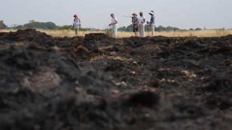 A group of walkers stop to look at the aftermath of a grass fire in Wanstead Flats, north-east London. The fourth heatwave of the summer will continue with temperatures expected to climb to 34C in parts of England. Picture date: Wednesday August 13, 2025. 