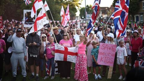 Large crowd of people waving Union Jack and St George flags outside council offices in Epping on 8 August 2025