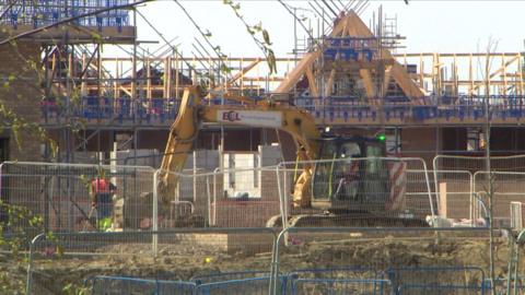 General view of housebuilding taking place, with a digger in the foreground.