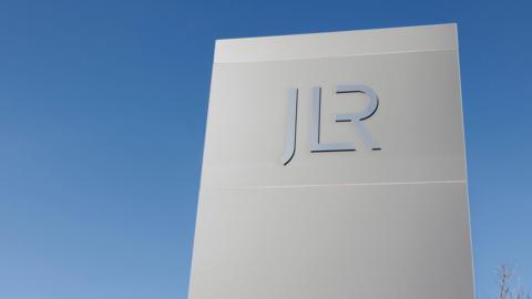 A large rectangular sign with the letters JLR against a blue sky