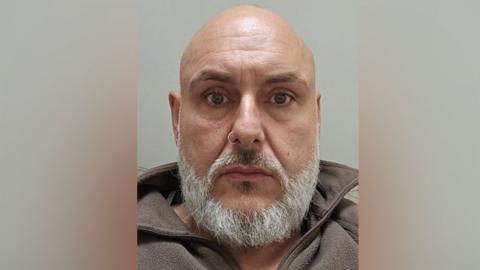Adrian Knott is looking into the camera. He has a bald head, grey beard and a nose ring. He is wearing a brown fleece top with the collar turned up.