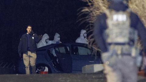 Investigators look at a grey Nissan car at a storage facility, where the Brown University shooter, identified by authorities, was found dead
