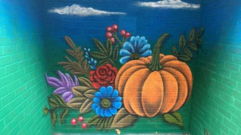 A painted mural inside a small brick structure showing brightly coloured flowers and a large pumpkin on a turquoise background