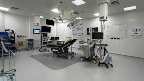 An operating theatre with equipment and a chair and several screens.