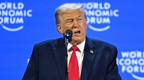 Trump in a red tie and blue jacket speaking at the world economic forum.