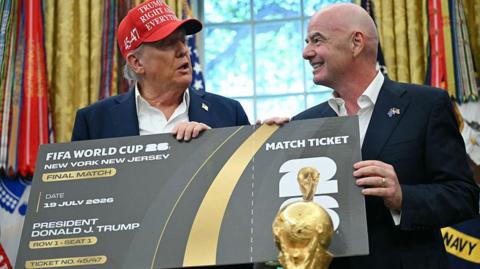 Donald Trump and Gianni Infantino are stood together in The Oval Office holding an oversized World Cup final ticket.