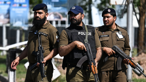 Close up of three security personnel standing guard at a security checkpost along a road temporarily closed near the Serena Hotel at the Red Zone area in Islamabad on April 20, 2026.