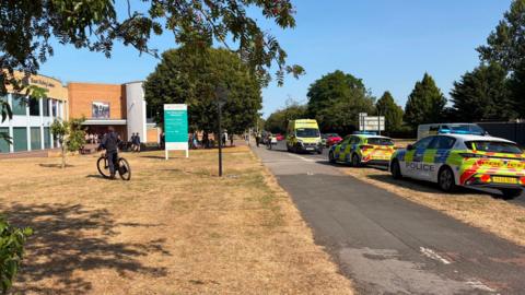 A line of police vehicles and an ambulance parked at the scene outside a leisure centre.