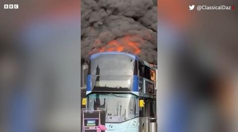 A bus with black smoke and flames coming from the top deck