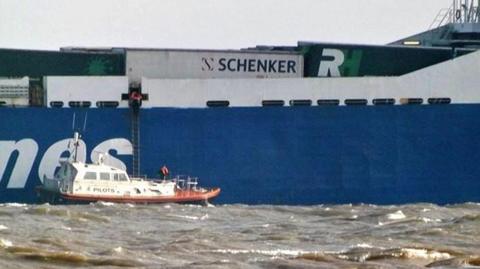 A small boat is situated in what looks like choppy sea next to a port with a ladder suspended from it which goes up into a larger platform.