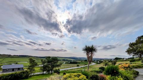 Hazy skies above green fields and shrubbery.  