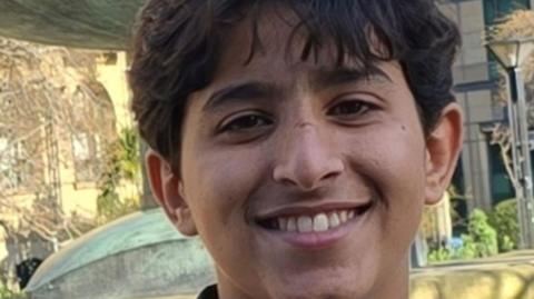 A teenage boy smiles in an outdoor setting.