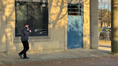 Christopher Ballard walking whilst lighting a cigarette