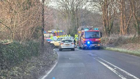 Emergency services including firefighters attend a crash in Newquay involving two cars. The fire engines at the scene have their blue lights on. Two cars, both silver, are on the road.