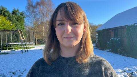 Crystal Owen is standing in front of a snowy garden. She has shoulder-length light brown hair and is wearing a grey knitted jumper