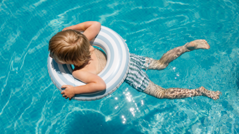 A child swimming in crystal blue water, he is in the middle of an inflatable ring.