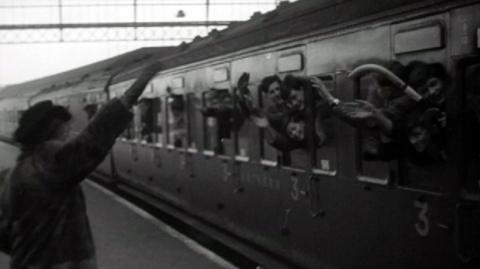 Children en route for boarding school wave through train windows.