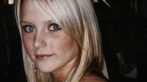 An 18-year-old girl with pale blonde hair and big eyes looking over her shoulder and smiling. She is dressed as for a night out.