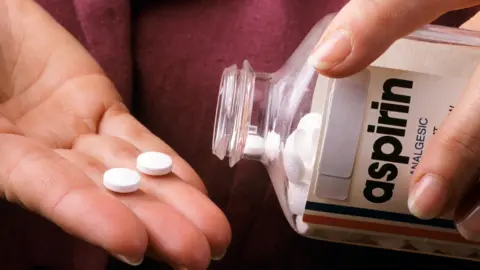 A close up of two aspirin pills on a hand, having been poured from a bottle in the other hand