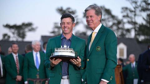 Rory McIlroy lifts the 2025 Masters trophy next to Fred Dibley in green jackets