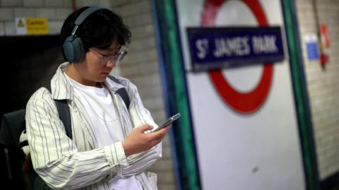 A man looks at his phone on the platform at St James' Park