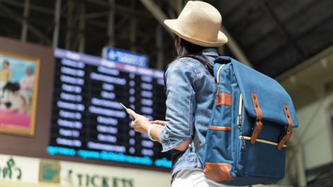 Woman holding phone while looking at departures boards