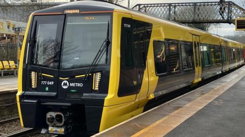 The Merseyrail train is black and yellow, and has stopped at a platform.