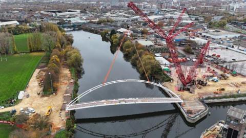 An aerial view of a large red crane lifting a large white bridge into place over the River Trent in Nottingham.