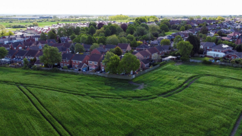 A drone view showing a large green field and houses - looking towards Ashton-in-Makerfield in Greater Manchester.