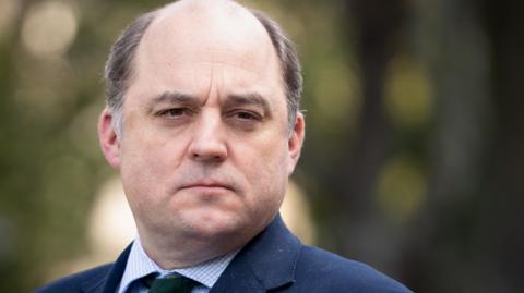 Man in suit and jacket looks at camera with serious facial expression