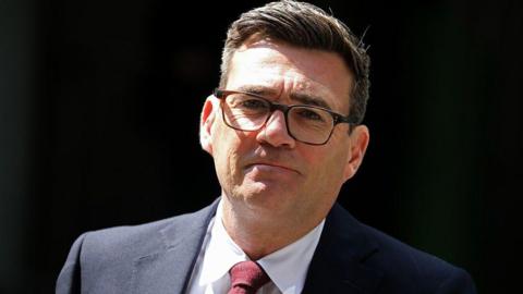 Andy Burnham, a white man with dark hair and glasses, in a blue suit and red tie.