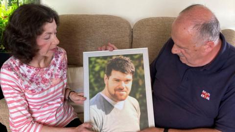 A man and a woman sitting holding a picture of their son