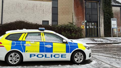 A police car sits outside Kirkwall Police Station, covered in snow. 