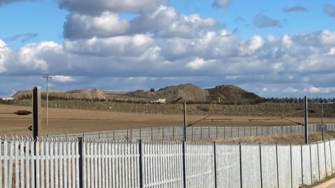 Shot of the tip, taken from afar behind a fence. Large brown mounts can be seen in the distance.