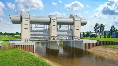 A computer-generated image of the flood barrier, over the river. It is a large structure made out of two main barriers above the water, with a bridge running along the width of it. The river level is low in the picture, and reinforced metal barriers are seen running along the side of the green river bank. 