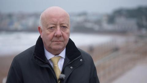 MP Steve Darling on Torbay seafront. He looks at the camera. He is wearing a yellow tie and black jacket