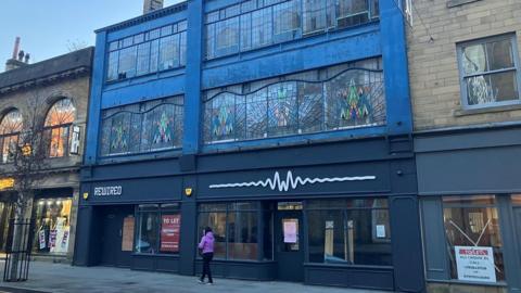 A photograph of the building shows the colourfully decorated windows stretching across the upper floor. An empty unit below has a "to let" poster fixed to the window.