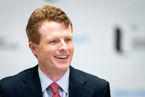 A close up of Joe Kennedy who has ginger hair. He is wearing a dark suit, light blue shirt and red tie