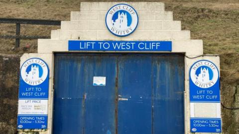 Blue doors which are closed. Signs read "Lift to West Cliff".
