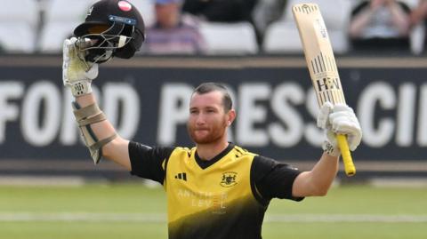 James Bracey raises his helmet and bat after reaching a hundred for Gloucestershire against Notts Outlaws