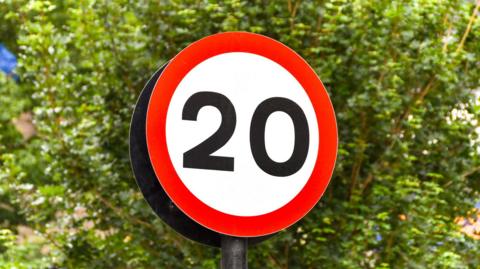 Stock image of a 20mph road sign. It is circular and has the number 20 in a white central section, surrounded by a red outline.