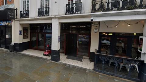 A white-fronted building with the entrance set back under the first floor. The letters VO are visible above the doors.