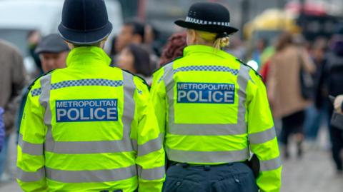 Two police officers are wearing yellow jackets with black hats