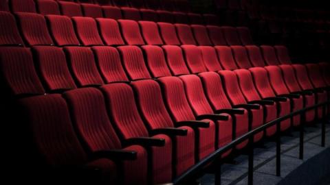A general view of red chairs in a theatre, with a bar in front of them.