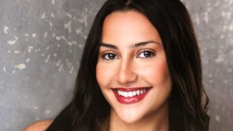 Rosa smiles at the camera in a professionally-taken headshot. She has long dark hair and wears bright red lipstick. 