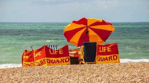 Red & yellow wind breaks & umbrella of the lifeguards on a summers day on a blue sky with white clouds background, Brighton, East Sussex,