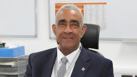 Paul Yates is wearing a dark suit and smiling at the camera while sat behind a desk. 