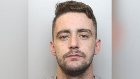 Police mugshot of Daniel Carter who has short dark hair and dark stubble.
