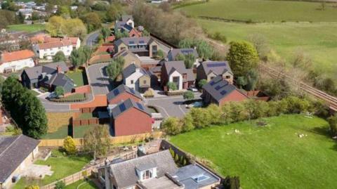 Artist's impression of a development of new homes, showing some green fields around the outside and a railway line running next to it.