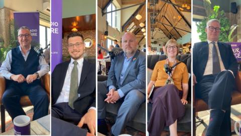 A row of people, four men and one woman, sitting on a sofa with microphones in front of them. They are looking at the camera and dressed smartly.